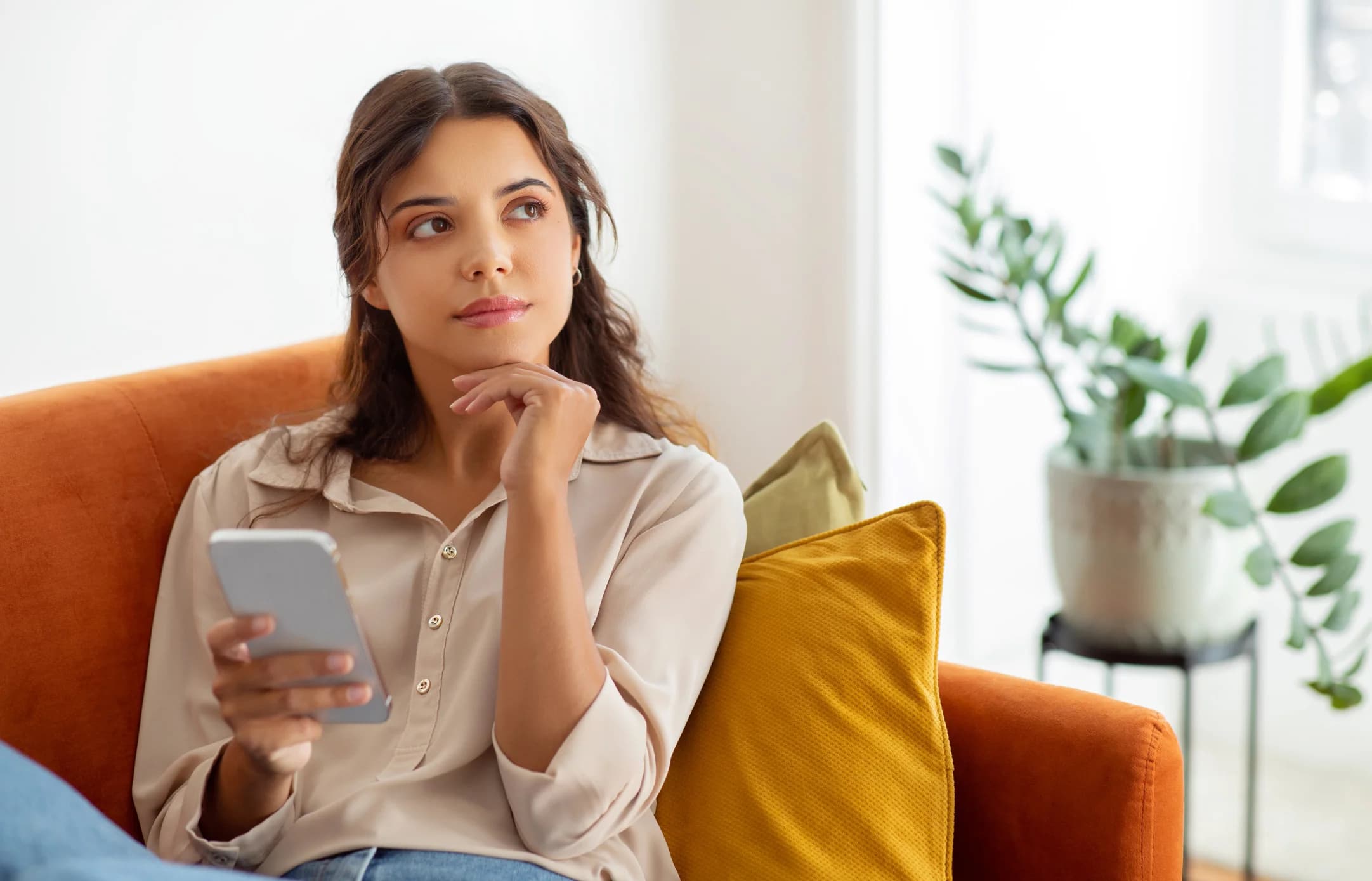 young woman holding smartphone deep in thoughts