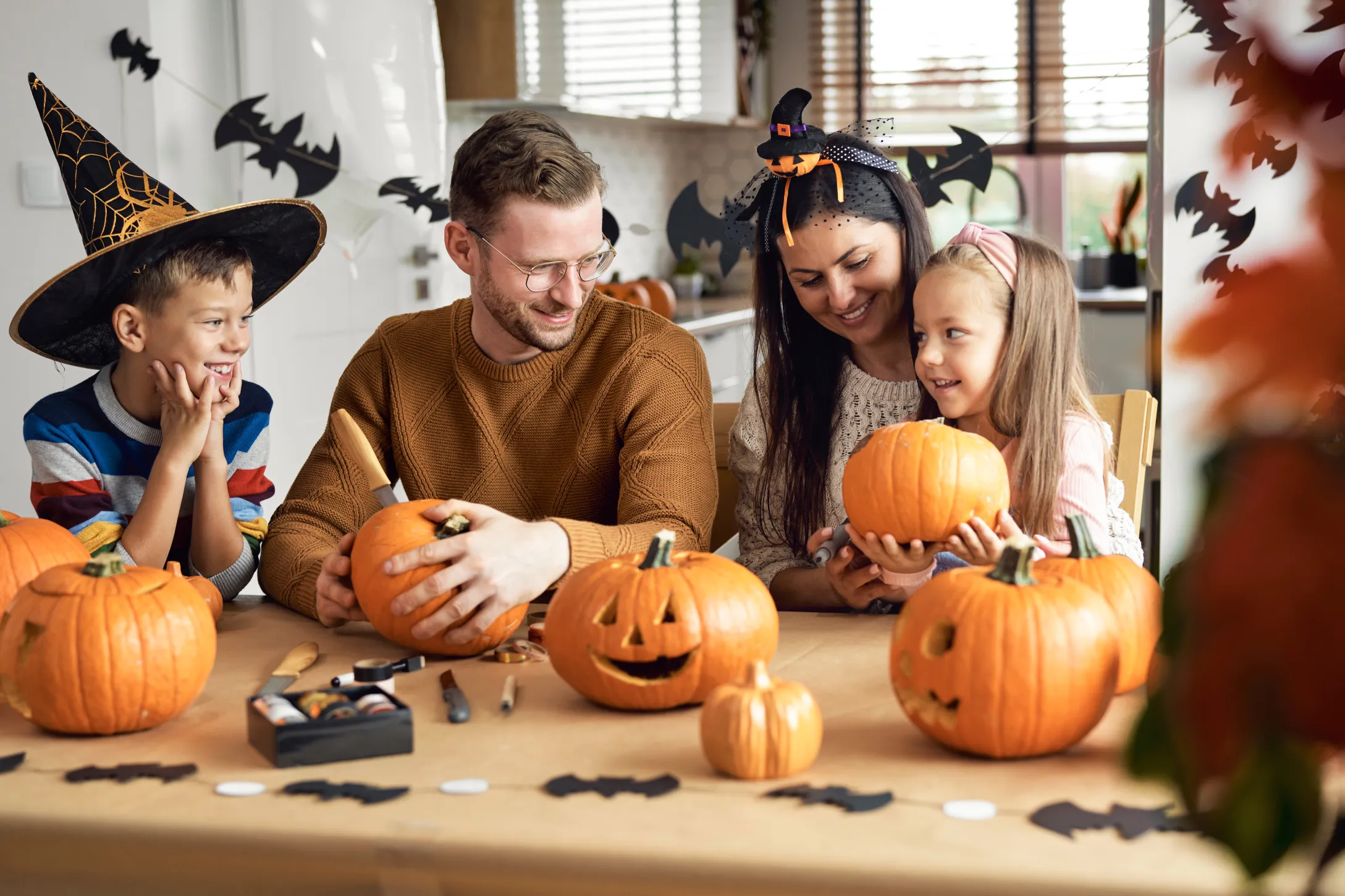 family-creating-diy-halloween-costumes-at-home-with-craft-supplies-and-pumpkins-on-table-demonstrating-affordable-halloween-budget-ideas-in-canada