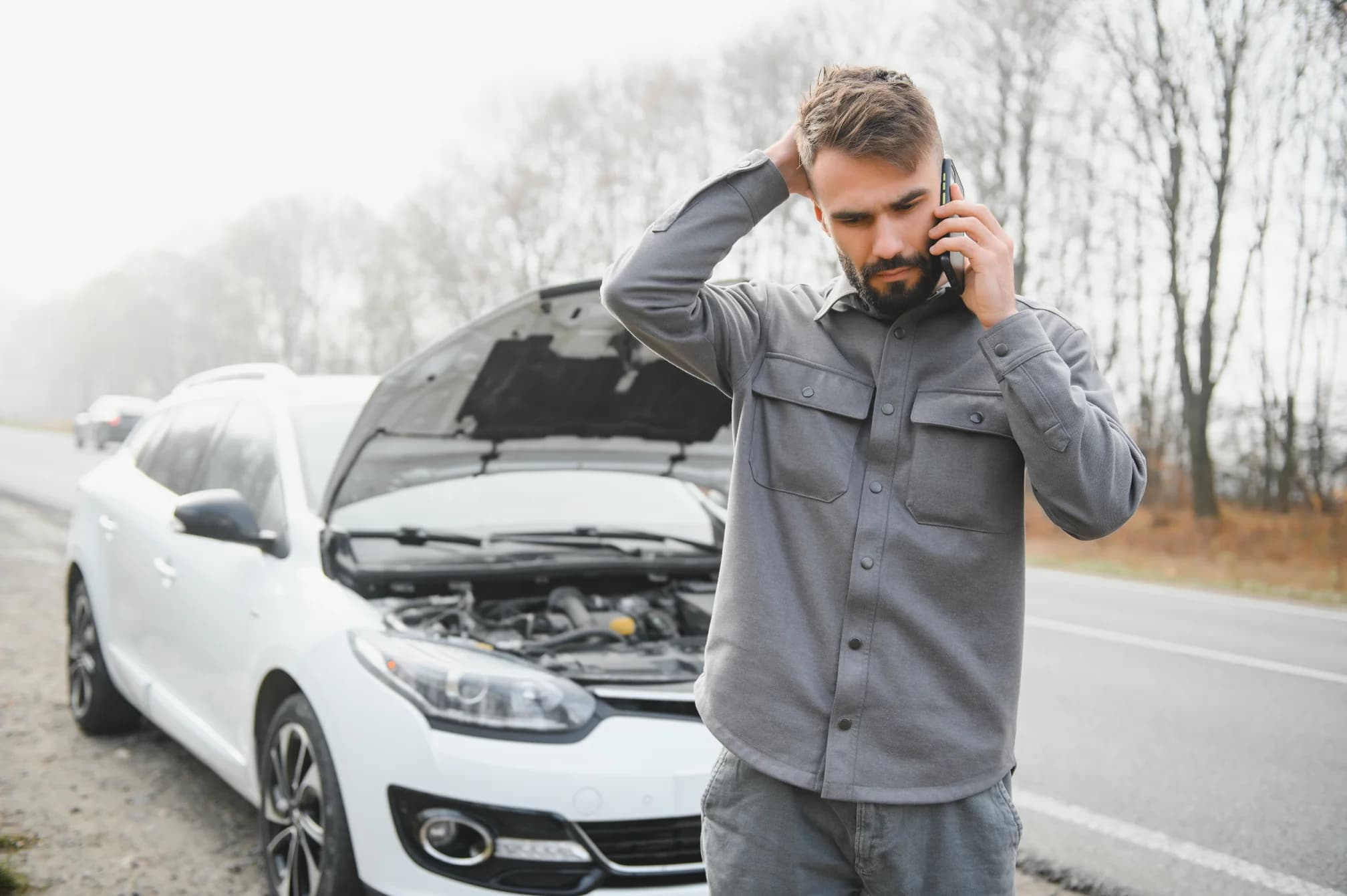Man use a cellphone in front of a broken car on the road